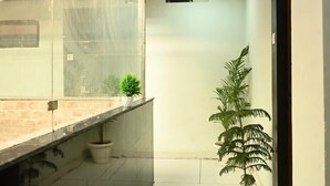 A corridor with a tiled floor, a potted plant, and a glass partition on one side. - HOTEL ROSHAN (Varanasi)