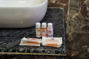 A bathroom counter with a white basin and three bottles of Hotel Roshan products. - HOTEL ROSHAN (Varanasi)