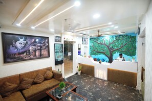 A reception area with a reception desk, a sofa, a coffee table, and a mural of a tree. - HOTEL ROSHAN (Varanasi)