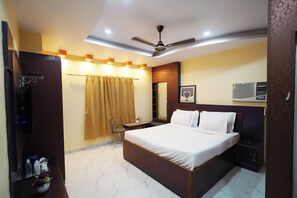 A hotel room with a bed, a desk, a chair, a ceiling fan, and a bathroom with a shower curtain.