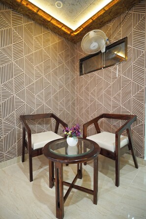 Una habitación con pared estampada, dos sillas de madera, una mesa de vidrio con un florero y un ventilador de techo.