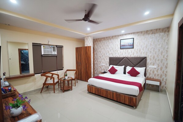 Une chambre d’hôtel équipée d’un lit, d’un bureau, d’une chaise, d’une armoire, d’un ventilateur de plafond et d’un climatiseur fixé au mur.