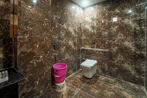 A modern bathroom with a marble wall, a glass shower enclosure, a white toilet, and a pink bucket on a pedestal.