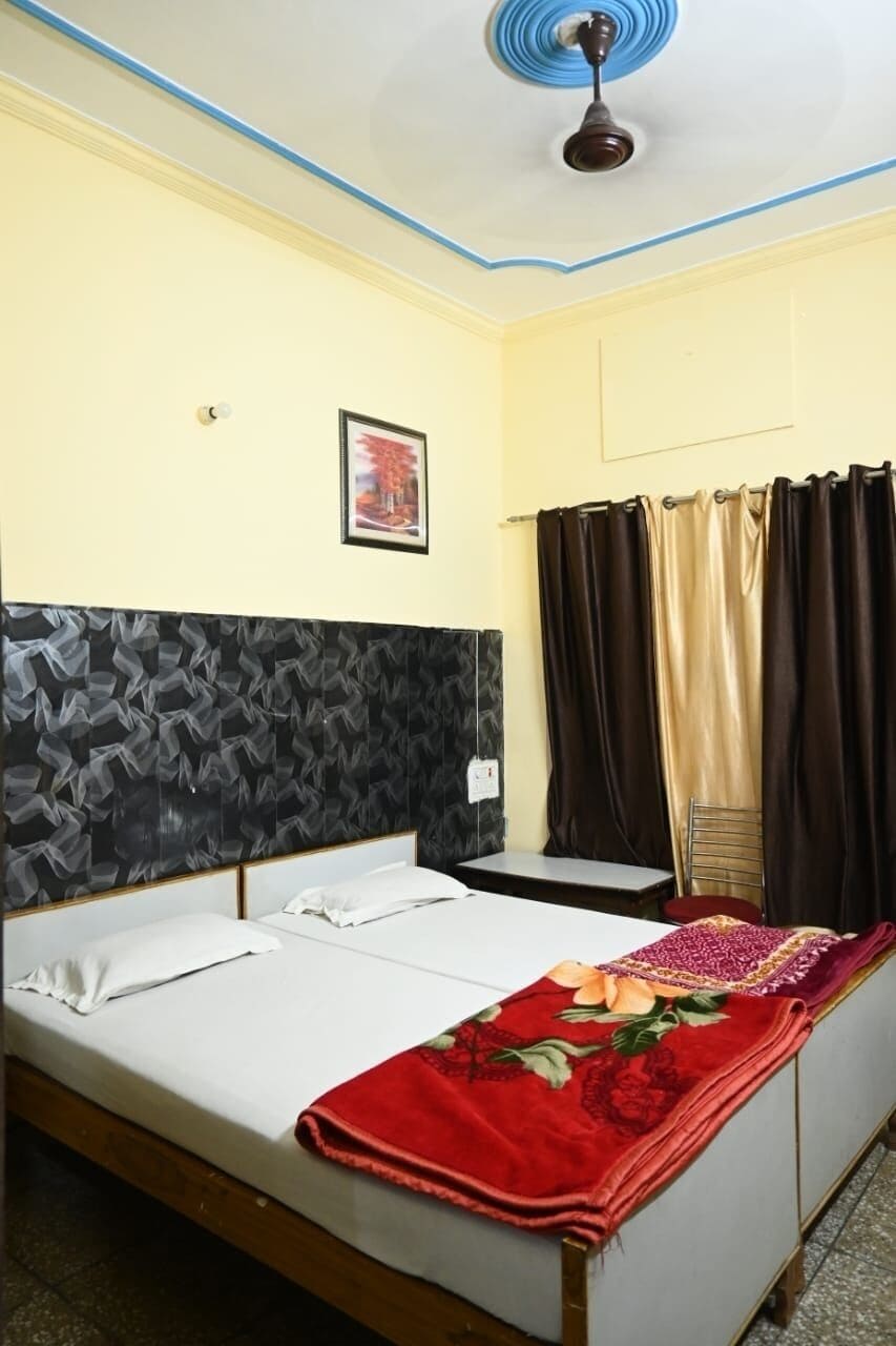 A room with a bed, a small table, a ceiling fan, and a window with curtains.