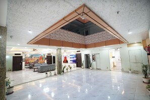 Un hall d’entrée spacieux avec un plafond haut, un coin salon et une variété de plantes en pot.