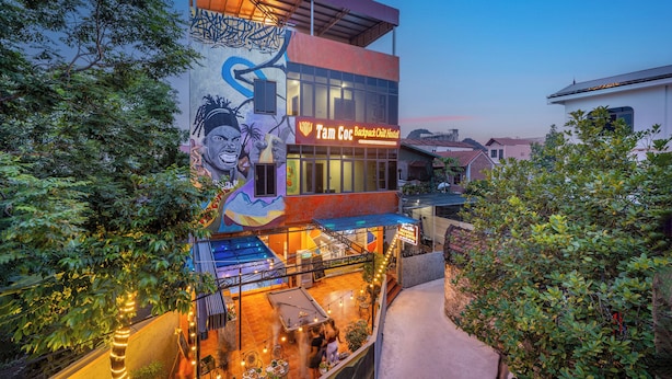 Un edificio con un murale, un cartello che riporta 'Tam Coc Backpack Child Hostel' e posti a sedere all'aperto.