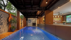 Area piscina con pavimento a scacchi blu, una reception e un muro con orologi e la insegna di un ostello.