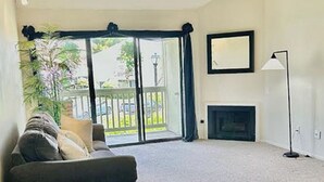 A living room with a sofa, a fireplace, and a large sliding glass door leading to a balcony. - Lovely 2/2 with optional 3rd bedroom condo one exit from the Del Mar Racetrack (San Diego)
