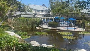 A pond with lily pads and a dock, surrounded by greenery and buildings in the background. - Lovely 2/2 with optional 3rd bedroom condo one exit from the Del Mar Racetrack (San Diego)