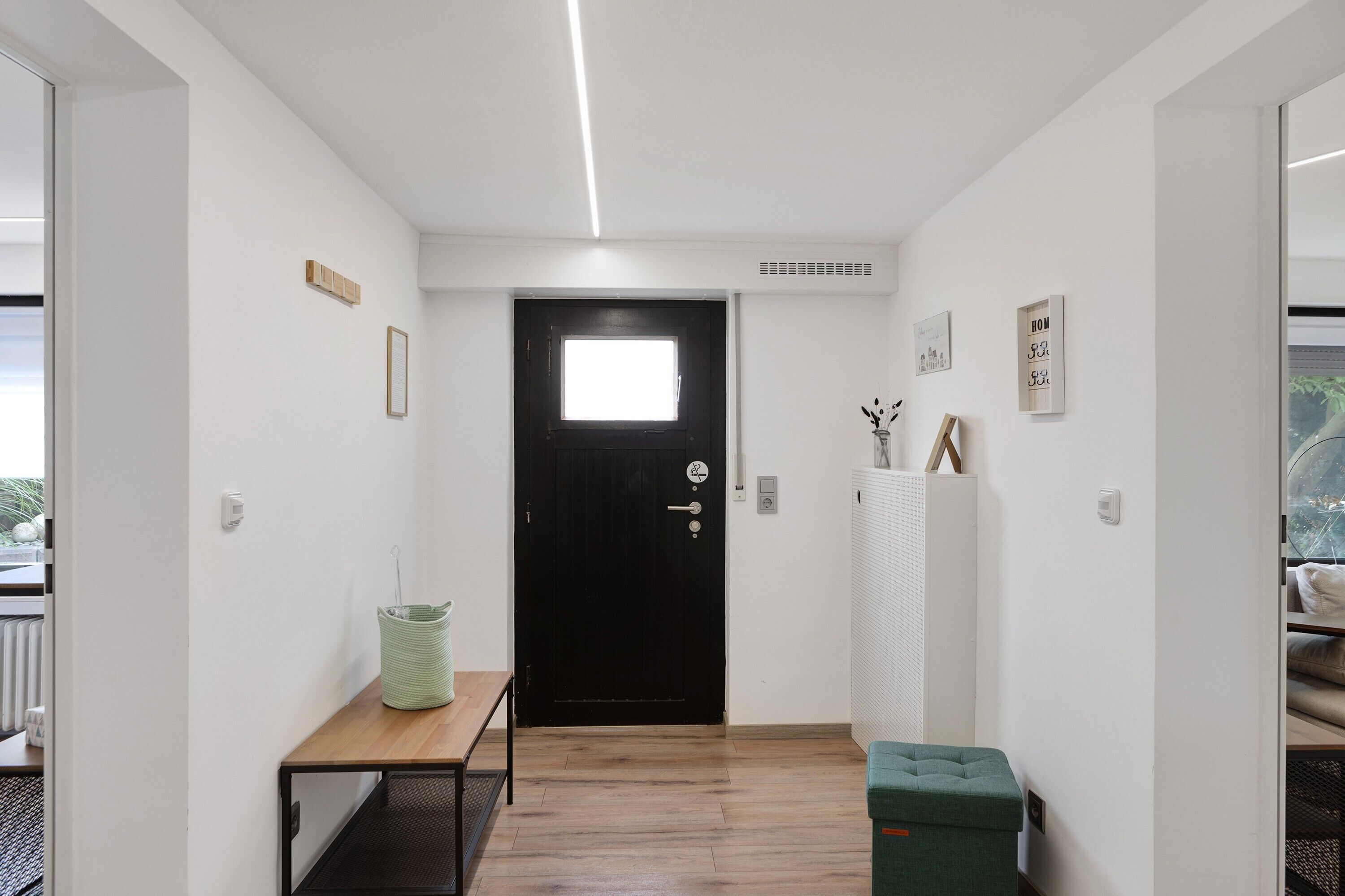 Un couloir avec une porte noire, une petite table, un panier vert et un radiateur.