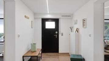 Un couloir avec une porte noire, une petite table, un panier vert et un radiateur.