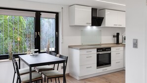 Una cocina moderna con armarios blancos, horno integrado y una zona de comedor con mesa y sillas.