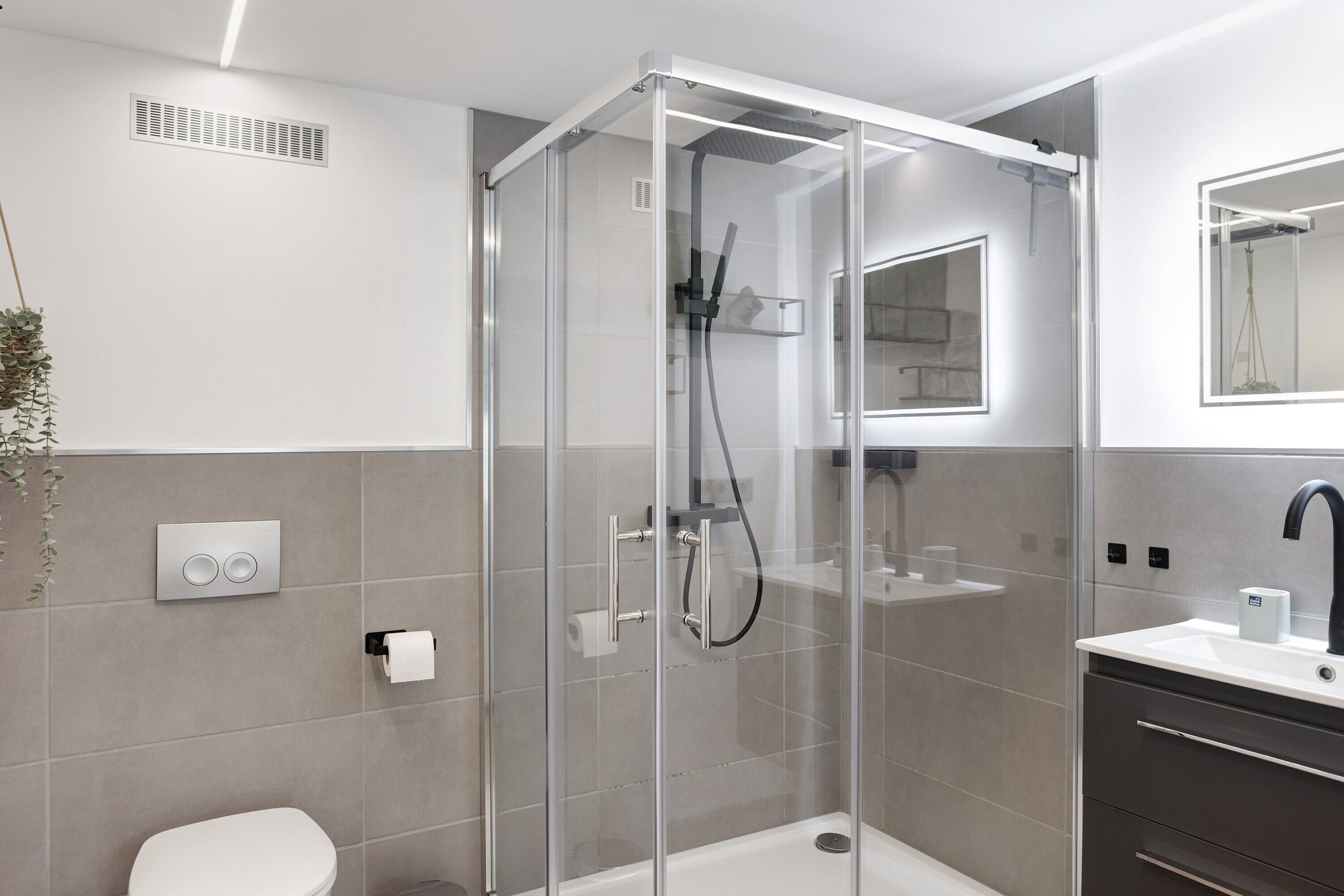 Un baño moderno con ducha de vidrio, inodoro, lavamanos con espejo y calentador de pared.