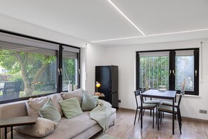 A modern living room with a sofa, dining table, chairs, a TV, and large windows. - Zentrumnahe ferienwohnung mit garten und stellplatz (Eschwege)