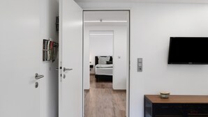 Una habitación de hotel moderna con cama, televisor montado en la pared y una puerta que da a otra habitación.