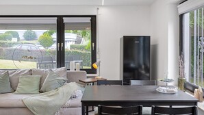 Una sala de estar moderna con un sofá, una mesa de comedor, sillas, un televisor y vistas al exterior.