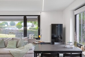 Un salon moderne comprenant un canapé, une table à manger, des chaises, un téléviseur et une vue sur l’extérieur.