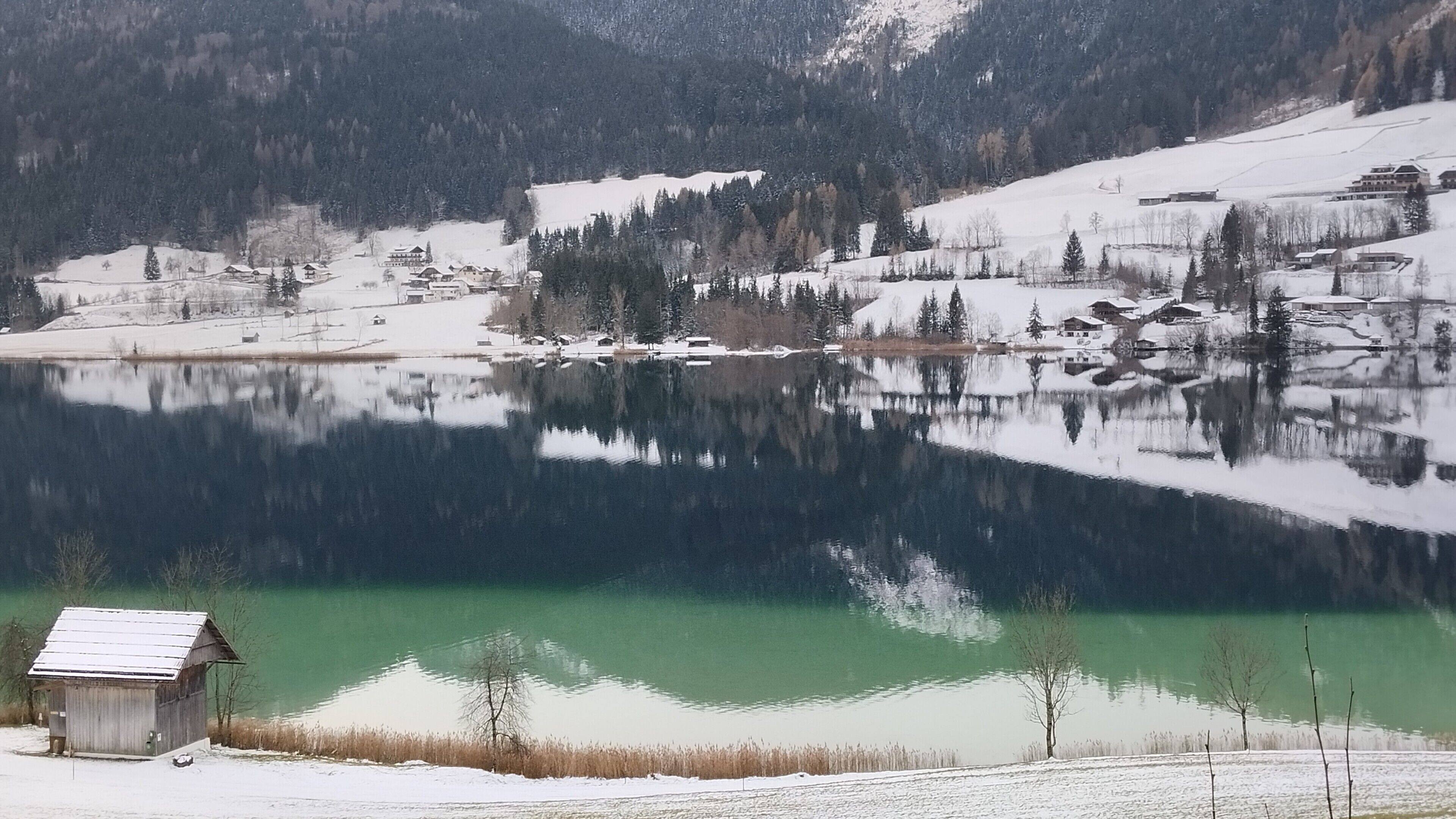 Un lac paisible, entouré de paysages enneigés, avec un petit bâtiment en bois en premier plan.