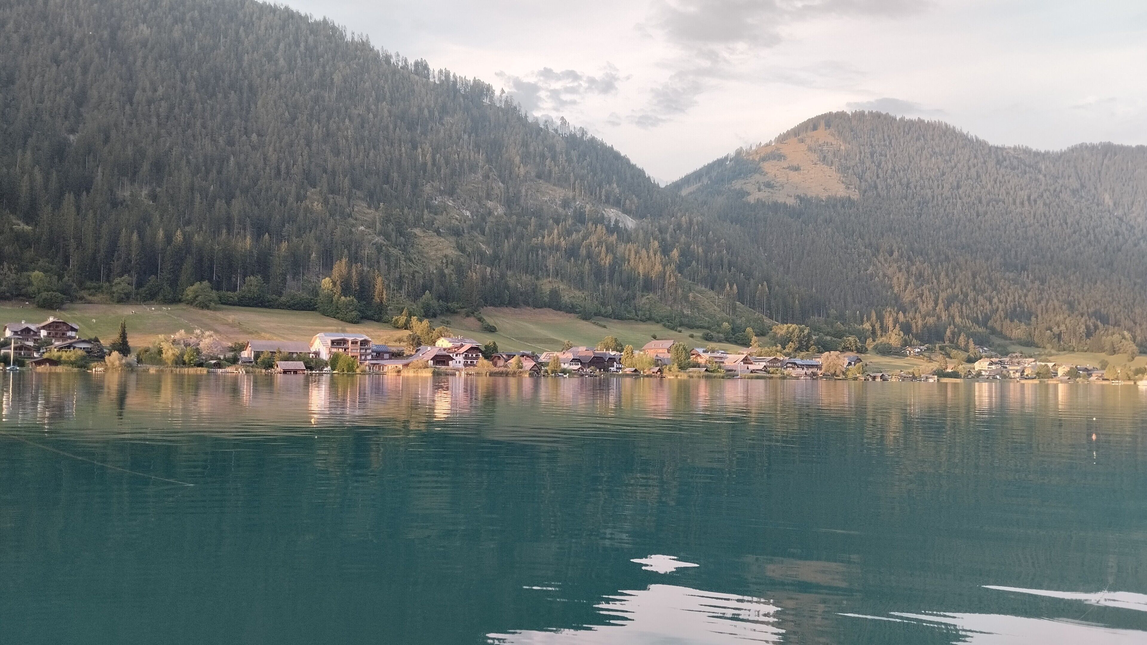A lakeside village with houses along the shore, surrounded by forested hills.