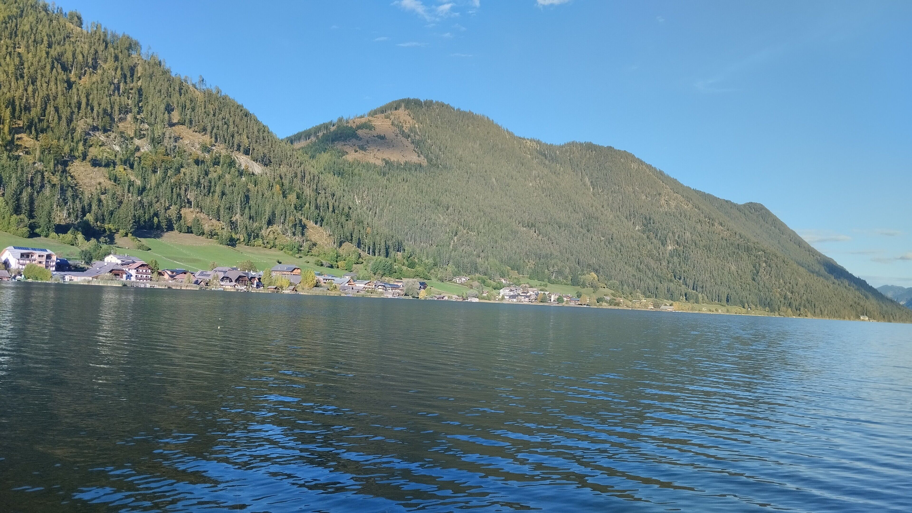 Vista para o lago, com uma montanha ao fundo e uma fileira de edifícios na orla.