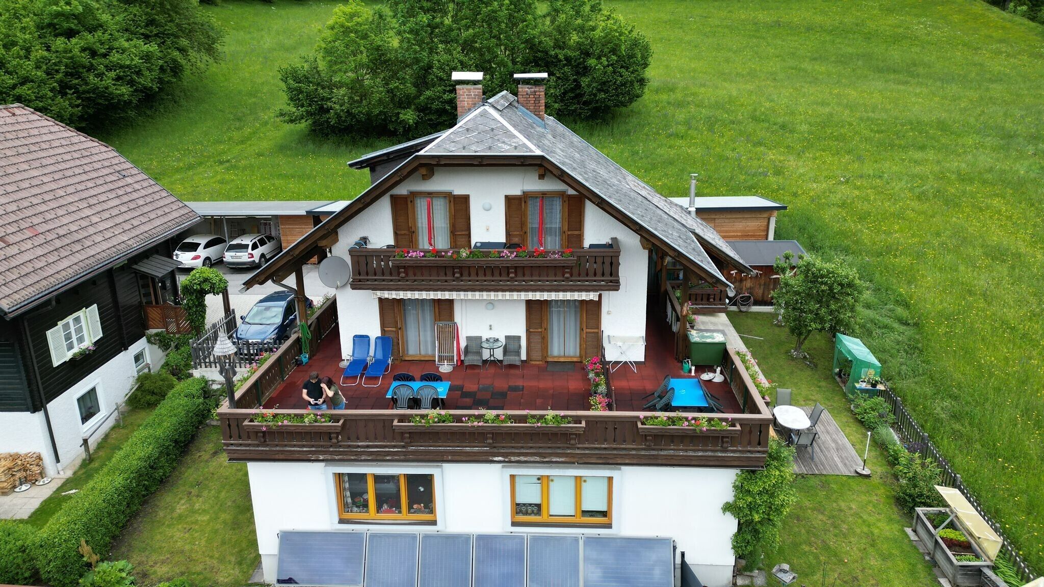 Une maison à deux étages avec un balcon, des panneaux solaires et un jardin.