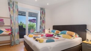 Ein Schlafzimmer mit einem Bett, einem Nachttisch, einer Lampe und einem Fenster mit Vorhängen.