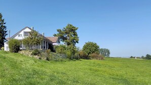 Ein weißes Haus mit rotem Dach, umgeben von einer grünen Wiese und Bäumen.