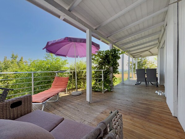 Un espacio al aire libre techado con una terraza de madera, una sombrilla morada, una silla de mimbre y una mesa con sillas.