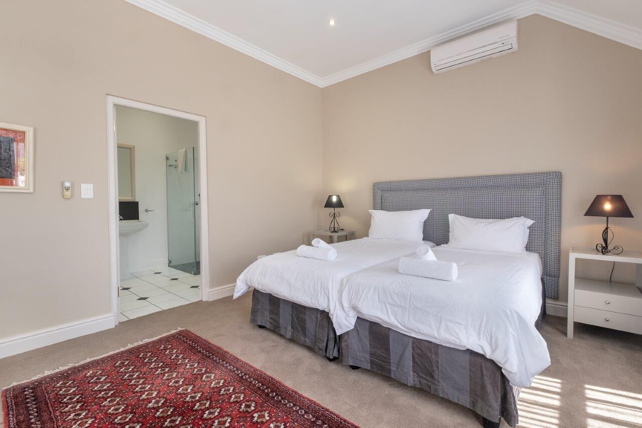 A hotel room with a large bed, a bedside table with a lamp, a red patterned rug, and a view of the bathroom through an open door.