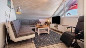 Un cuarto tipo loft con techo inclinado, un sofá, una mesa de centro, un televisor, una silla y una ventana con vistas.