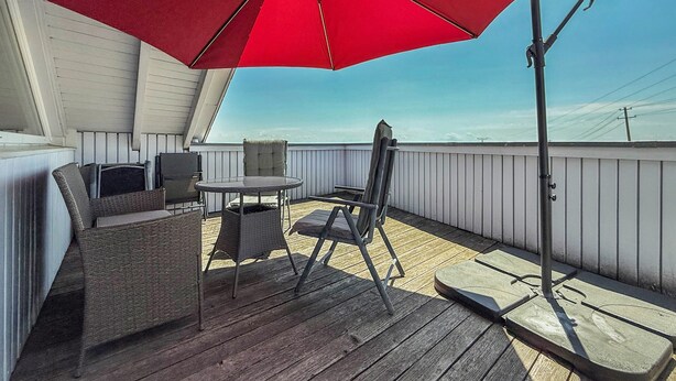 Una terraza techada al aire libre con un paraguas rojo, muebles de mimbre y vista al cielo.