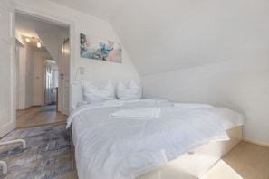 Una camera da letto con un letto, pareti bianche, un quadro e un corridoio che porta verso un'altra stanza.