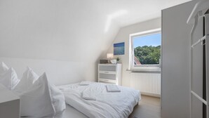 A bedroom with a bed, a window, a radiator, and a shelf with items. - Apartment 'Steilküste' with Private Terrace, Private Garden and Wi-Fi (Lübeck Travemünde)