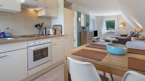 A modern kitchen with a stove, oven, and dining area with a table and chairs. - Apartment 'Steilküste' with Private Terrace, Private Garden and Wi-Fi (Lübeck Travemünde)