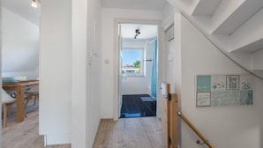 A hallway with a wooden staircase, a dining area with a table and chairs, and a view of the outside. - Apartment 'Steilküste' with Private Terrace, Private Garden and Wi-Fi (Lübeck Travemünde)