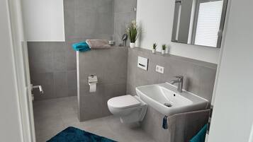 Un bagno moderno con doccia, servizi igienici, lavandino e un piccolo specchio.
