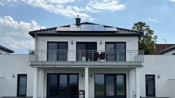 Et moderne hus i to etager med balkon, store vinduer og solpanel på taget.