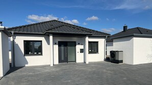 En moderne bygning med tegltag, garageport og et lille udendørs område med en skraldespand.