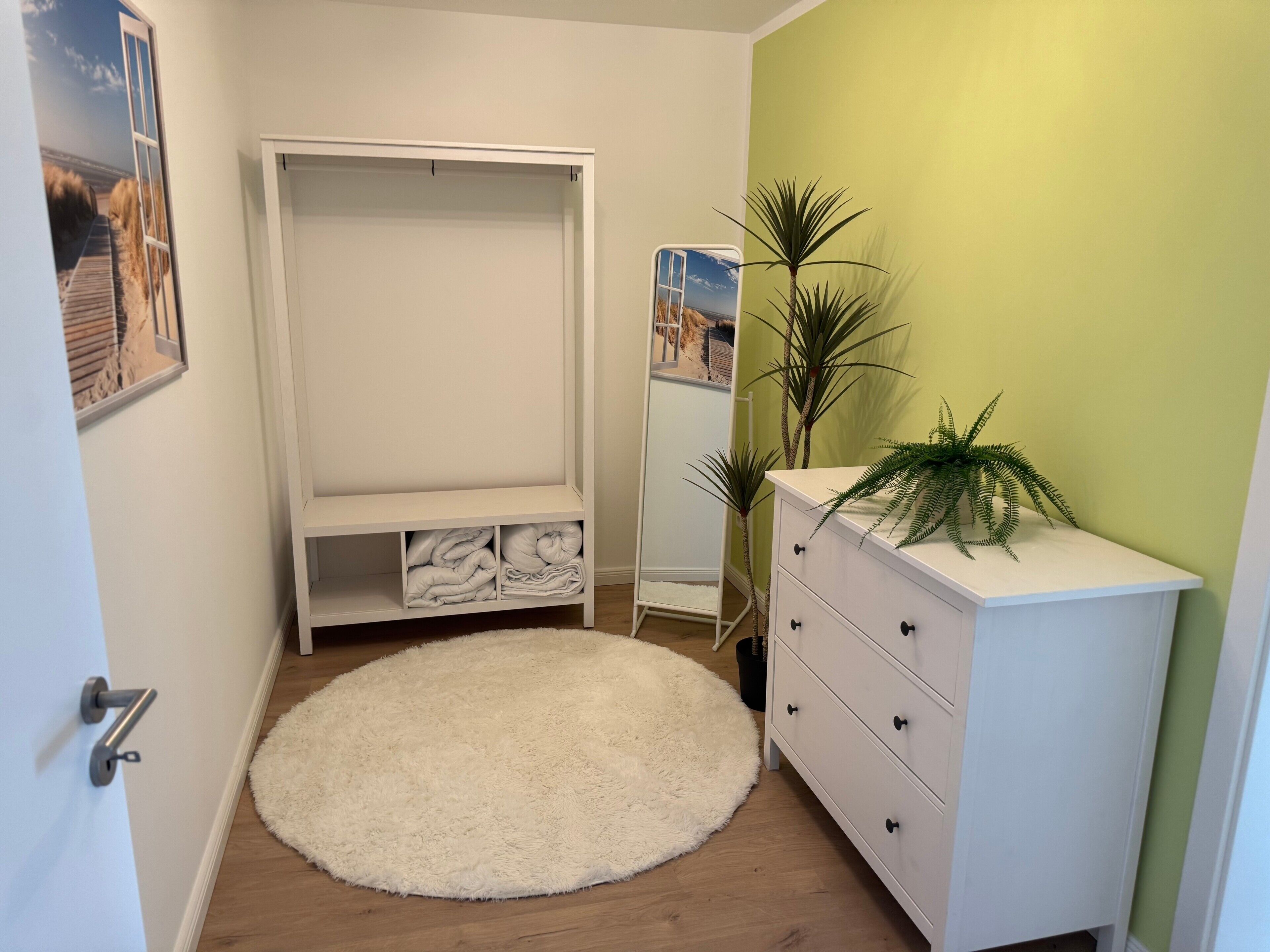 A room with a white wardrobe, a round white rug, a white dresser, and a green wall.
