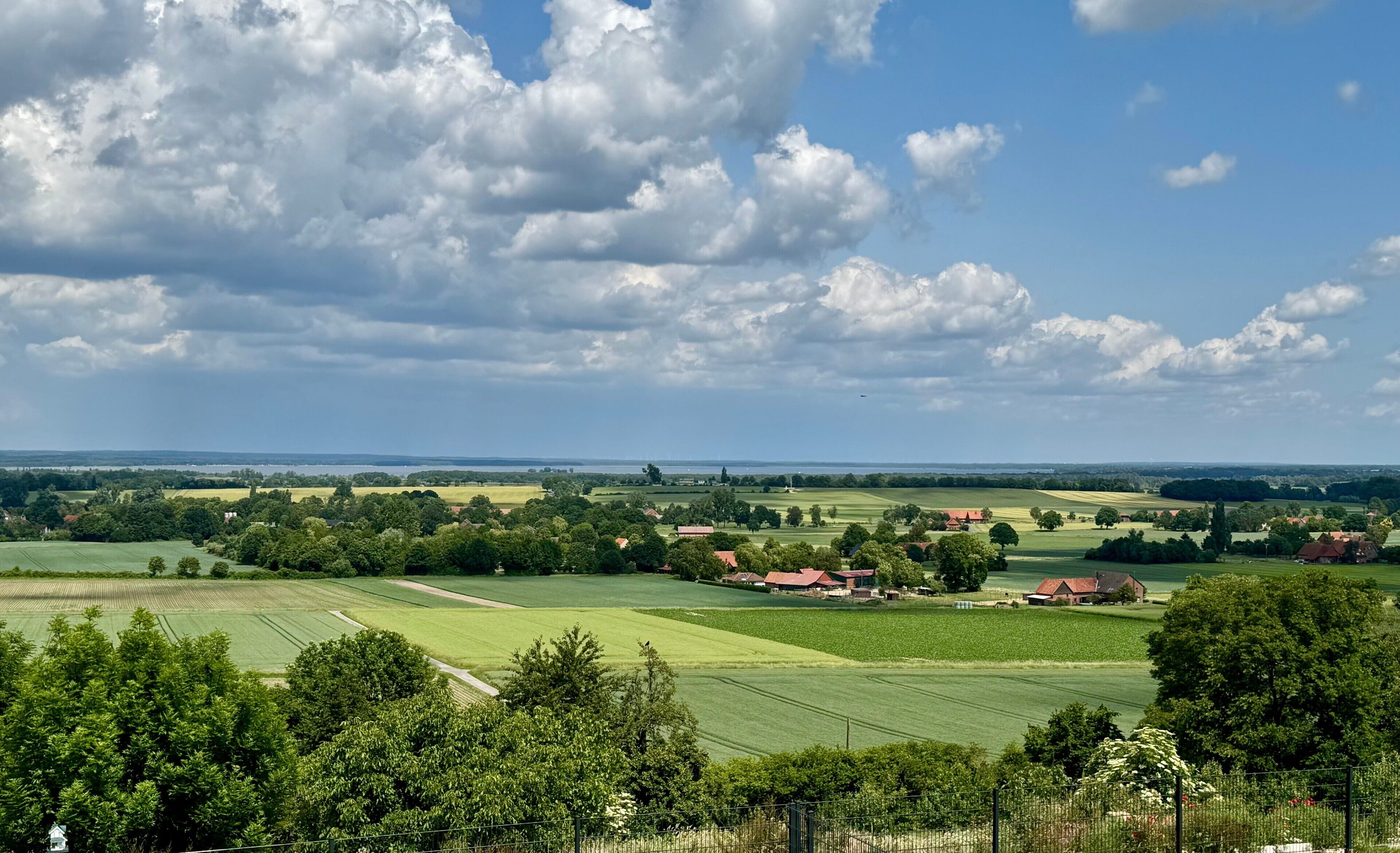 Un paysage rural composé de champs, d’arbres et de quelques maisons dispersées.