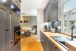 A modern kitchen with grey cabinets, a wooden countertop, a built-in oven, and a window with a view of buildings.