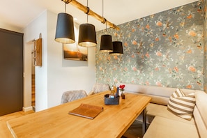 A dining area with a wooden table, three hanging pendant lights, a floral wallpaper, and a sofa with striped pillows.