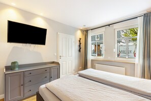 A bedroom with a bed, a dresser, a flat-screen TV, and a window with a view of the street.