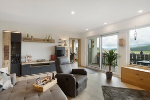 Ein modernes Wohnzimmer mit einer Couch, einem Liegestuhl, einem Holztisch und einer Zimmerpflanze.