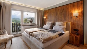 A bedroom with a large bed, a wooden accent wall, a nightstand, a chair, and a view of the outdoors.