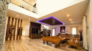 Een ruime woonkamer met houten vloer, een houten bank, een televisie en een balkon met hekwerk.