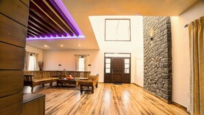 Een ruime woonkamer met houten vloer, een accentmuur van steen en een modern plafondontwerp.