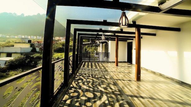 Een overdekt balkon buiten met patroon vloer, metalen hekwerk en hangende lampen.
