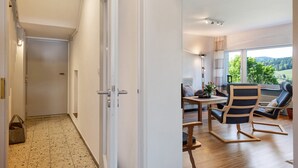 Un interno moderno con un corridoio che conduce a una stanza vista, una zona pranzo con tavolo e sedie, e un’area salotto con poltrona e divano.