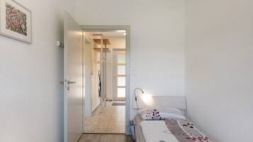 Een slaapkamer met een bed, een bedlamp, een deur naar een gang en een lijst met een afbeelding aan de muur.